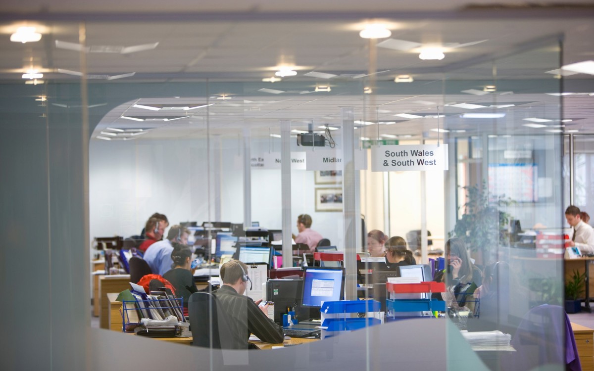 A busy office environment with people sat at desks in front of computers screens with headsets