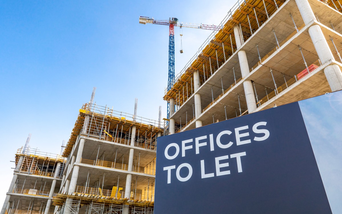 High rise office units under construction. There is a dark blue sign with white text reading Offices To Let. In the midground are the buildings under construction, we look up from a low angle and can see four floors. In the background there is a crane.