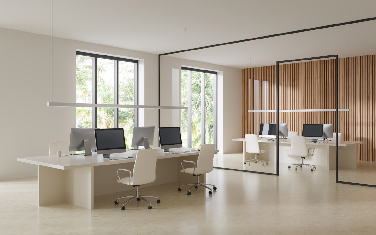 An empty office space, minimal decor, lcd screens on shared desk space, white chairs, wood panelling, tall windows bathe the room in natural white light.