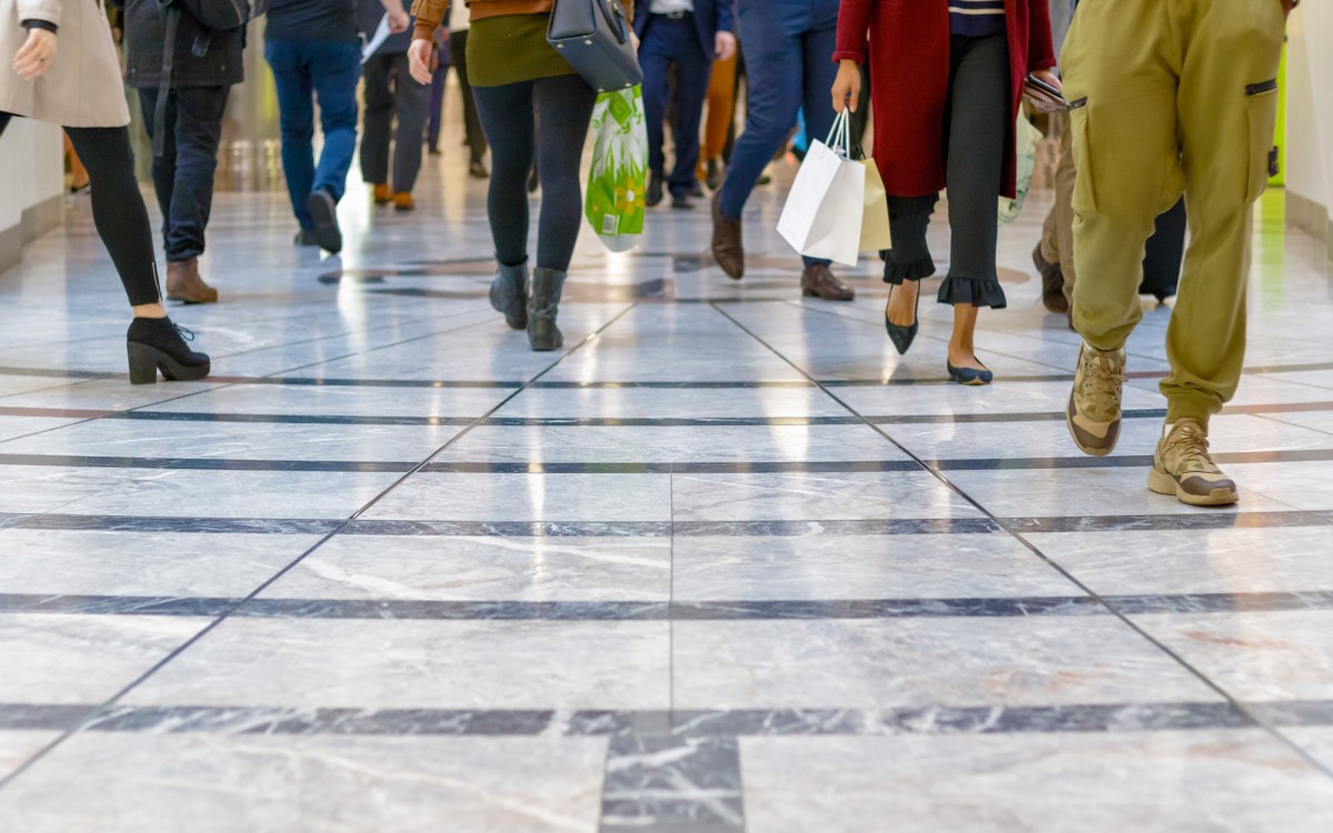 People walking on a marble effect floor in a shop centre, everyone is walking in different directions and carry bags